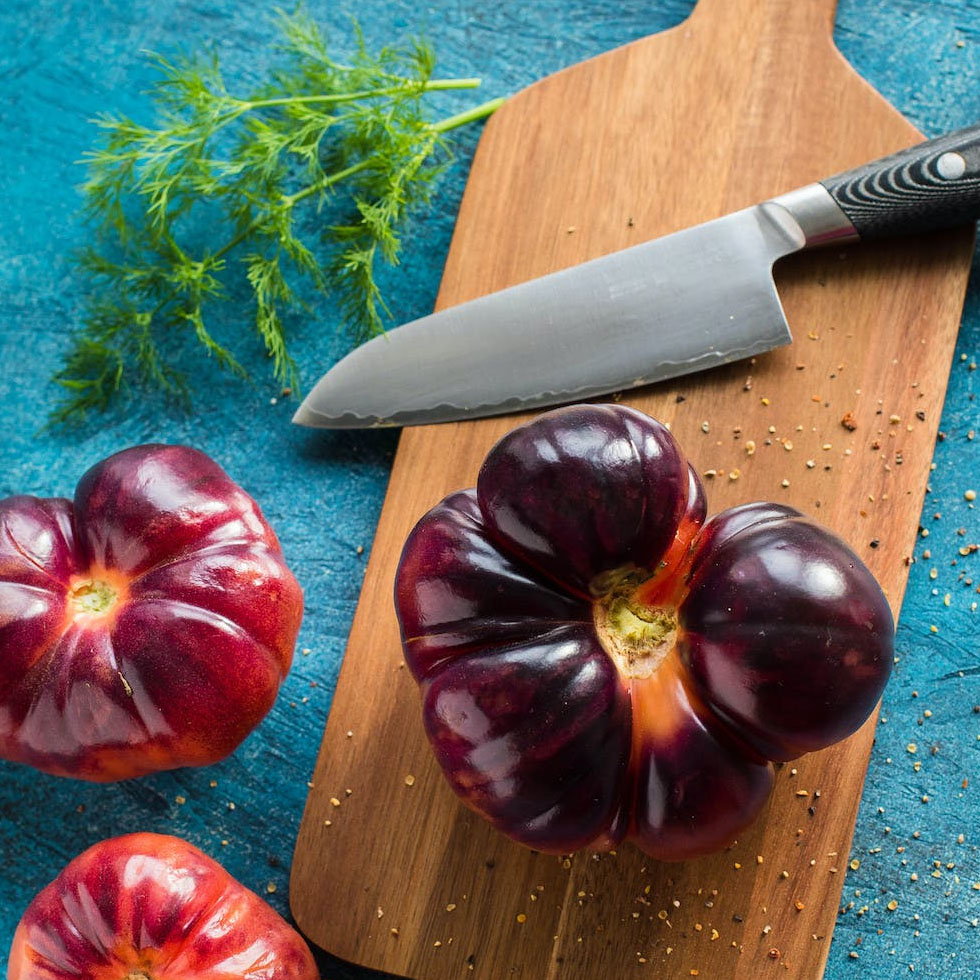 tabla de cortar de madera con cuchillo afilado y tomates negros